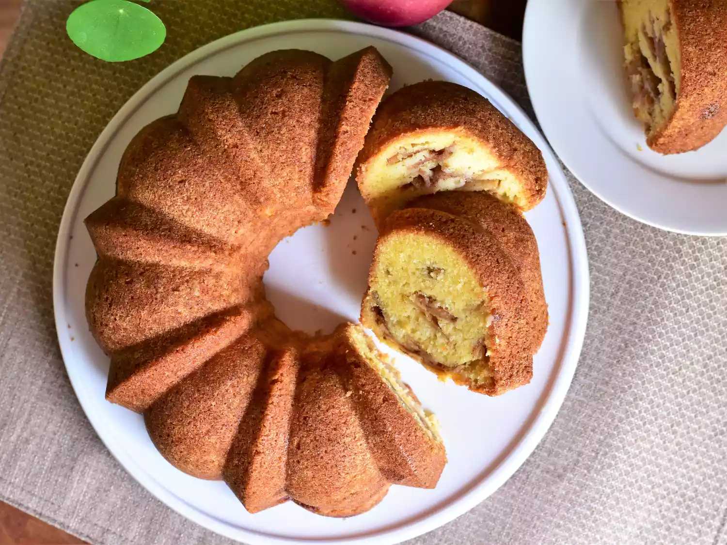 نمای بالا از کیک سیب پخته شده در قالب میان تهی با برشی از کیک - طرز تهیه کیک سیب